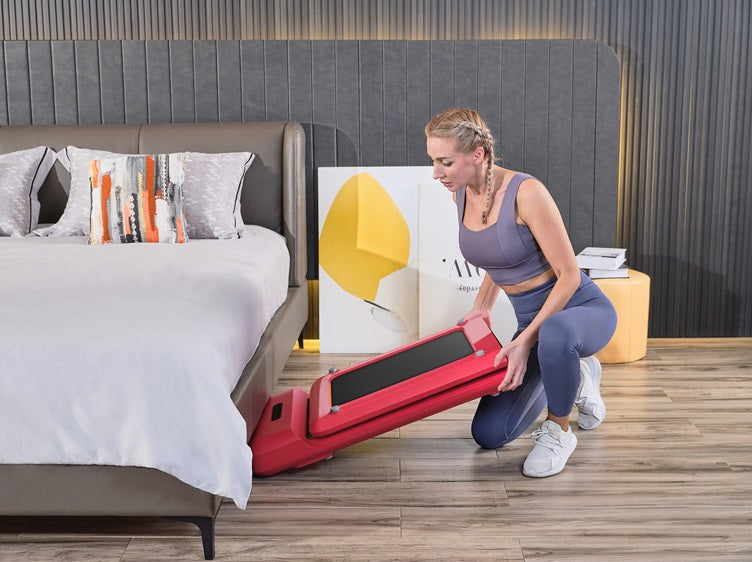 Woman folding a walking pad and placing it under a bed for space-saving storage