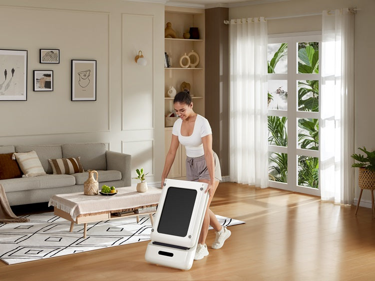 Woman storing a foldable treadmill in a bright, modern living room with minimalist decor